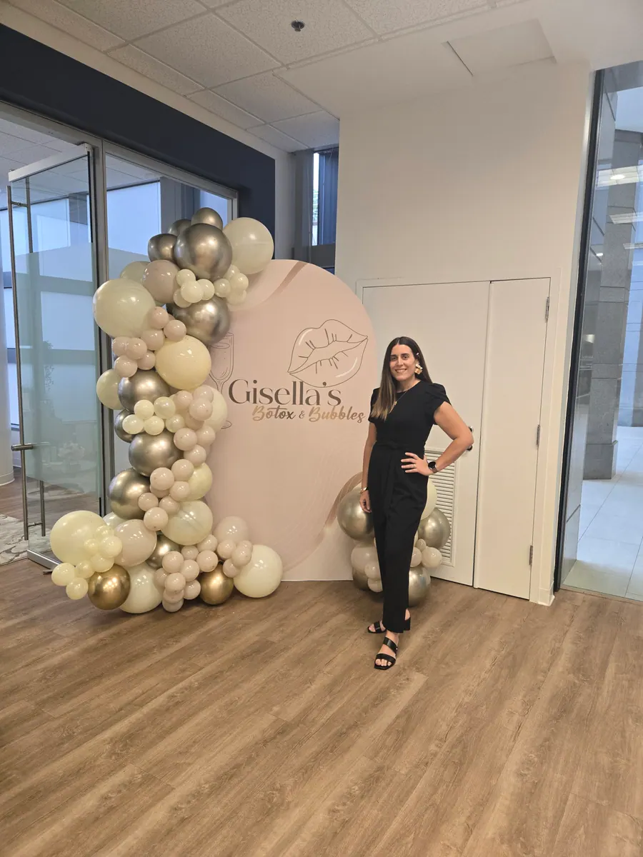 A host beside the balloon arch at an Esthetica Botox & Bubbles event
