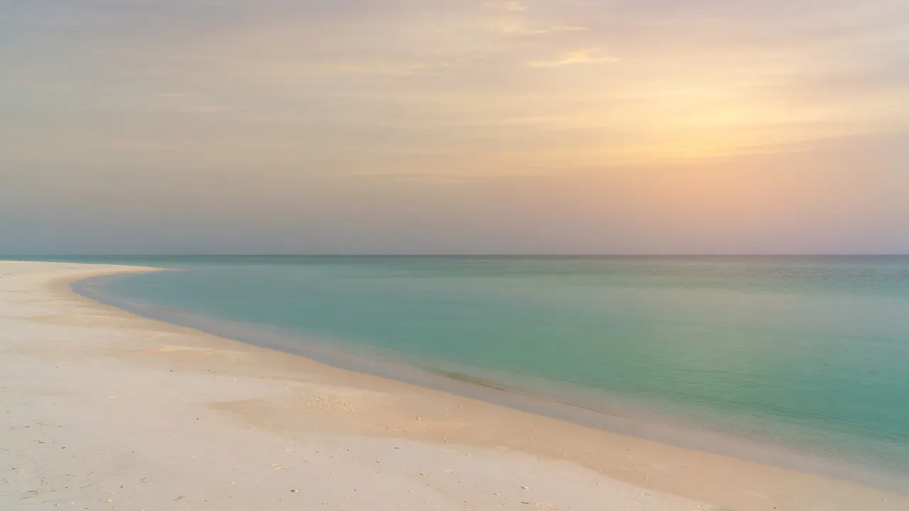 Empty sugar-sand Gulf beach at dawn, glassy turquoise water meeting a hazy pastel sky