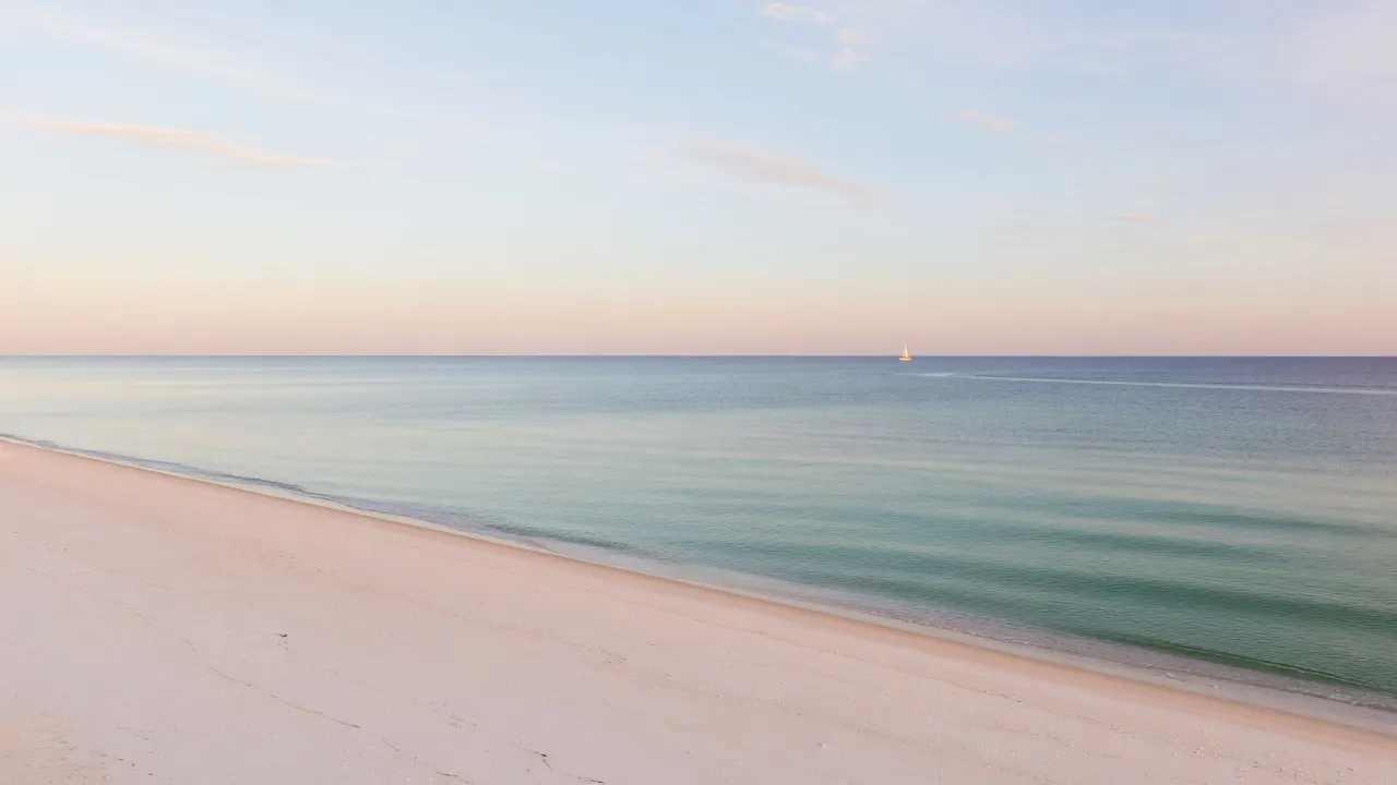 Wide Gulf coast at dawn: empty sugar-sand beach, calm turquoise water, vast pale sky, one faint distant sail on the horizon